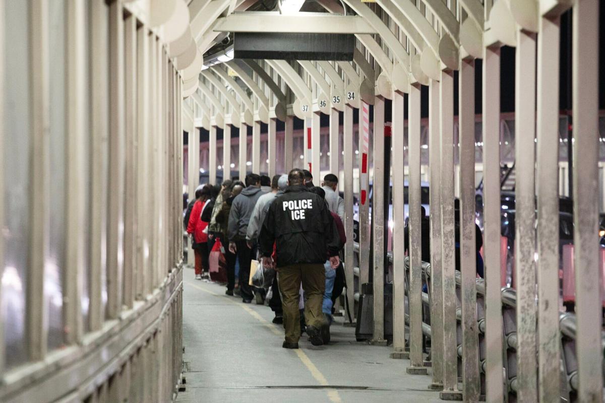 An ICE agent escorts a group of men being deported
