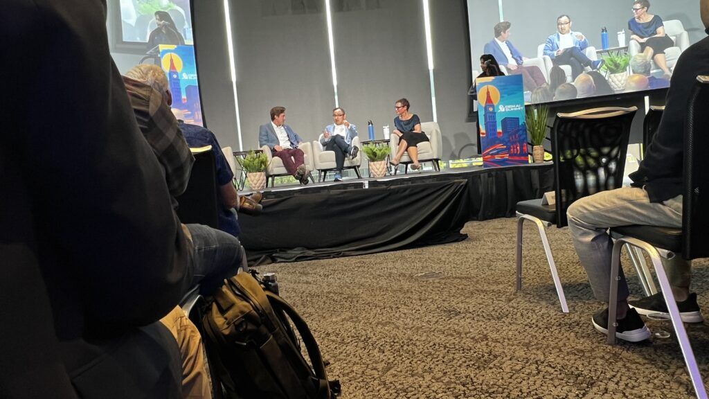 a crowded hall with athree pople on a stage.