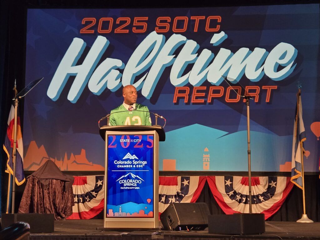 Colorado Springs Mayor Yemi Mobolade stands in front of a screen saying "2025 SOTC Halftime Report"