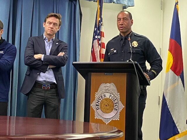 a uniformed police officer stands behind a podium as a city official looks on