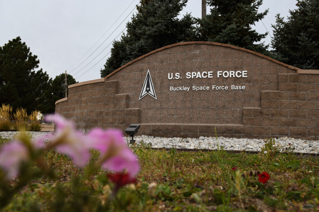 A sign that reads Buckley Space Force Base with pink flowers in the foreground.