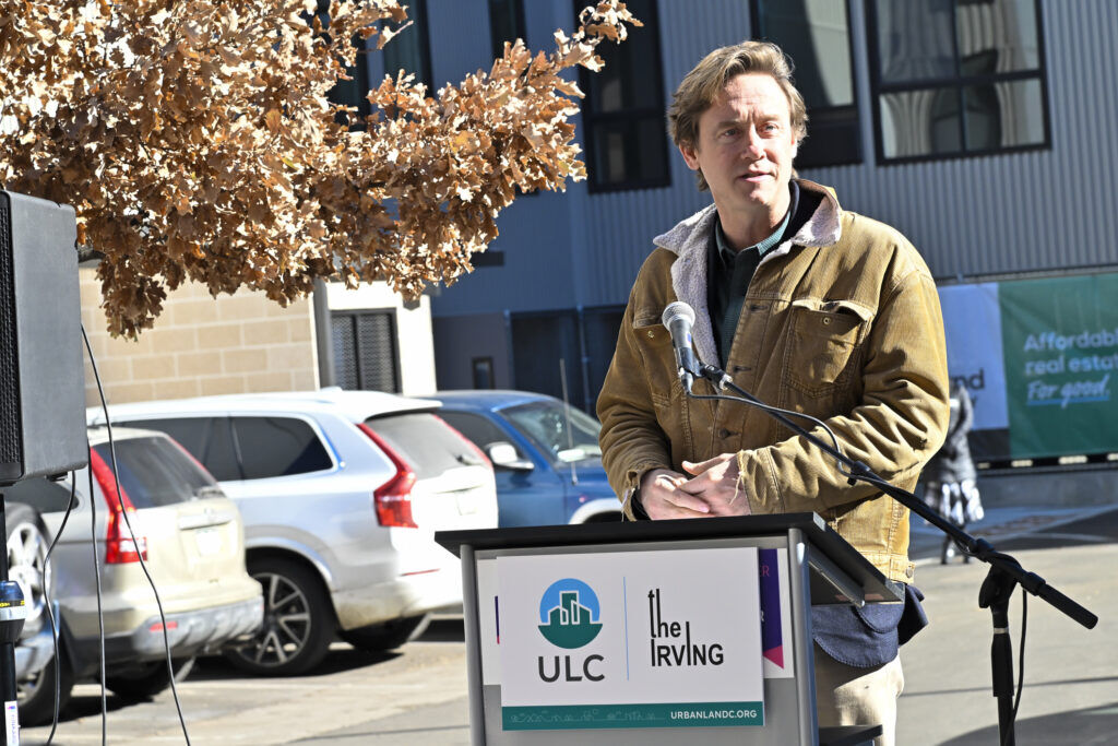a man in a brown jacket standing behind a podium