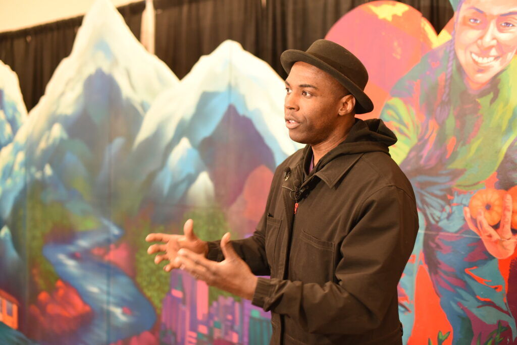 A man speaks in front of a mural