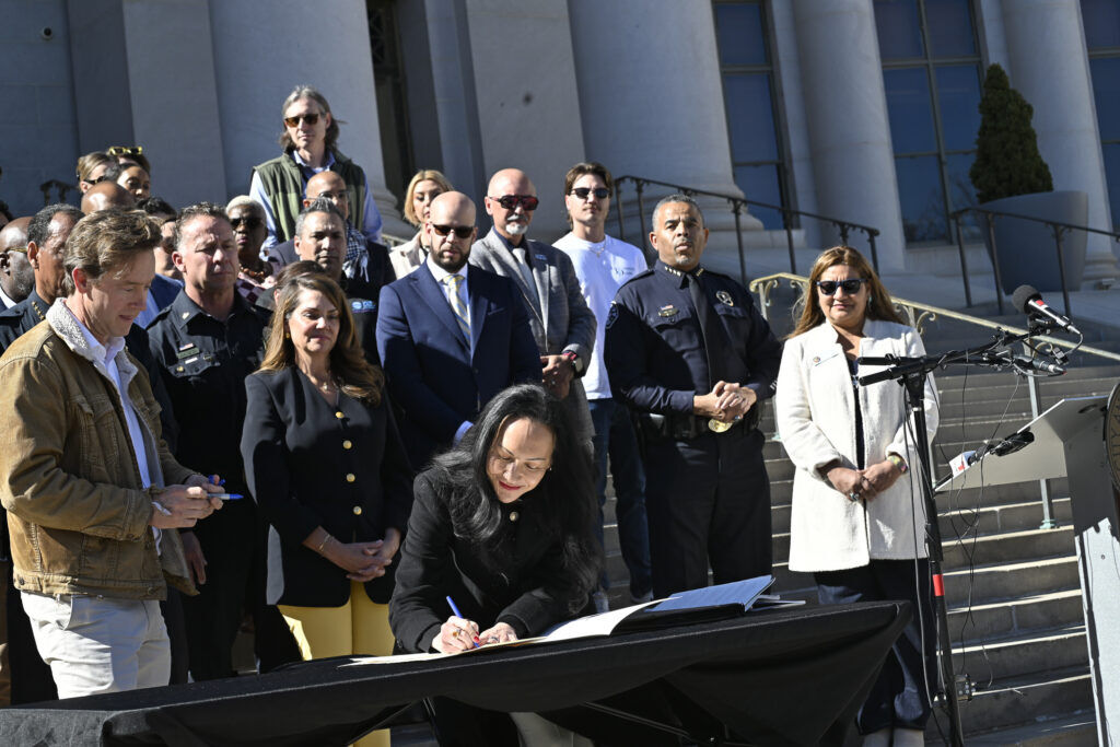 a woman signs an official document as a many looks on