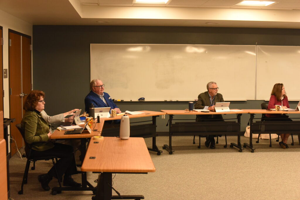 Several people sit behind a table under florescent lighting