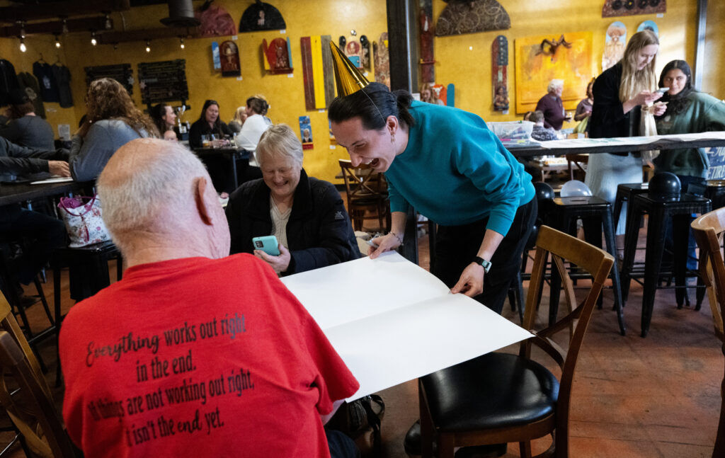 A person passing around a novelty-sized retirement card for people to sign