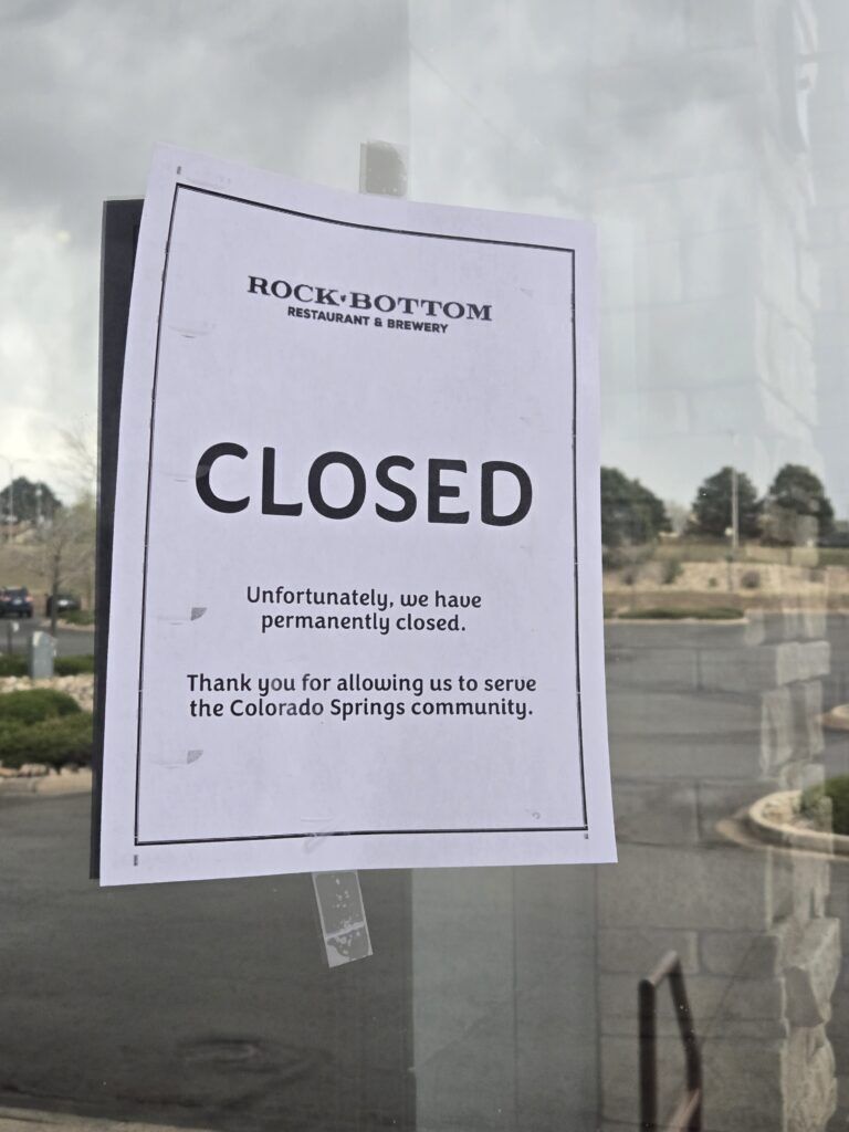 A white paper sign featuring the Rock Bottom Restaurant & Brewery logo on the masthead, alerts customers that the restaurant and brewery is permanently closed.