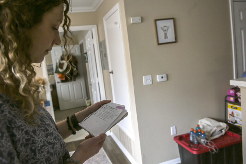 a woman looks over a list she made in a small spiral-bound notebook