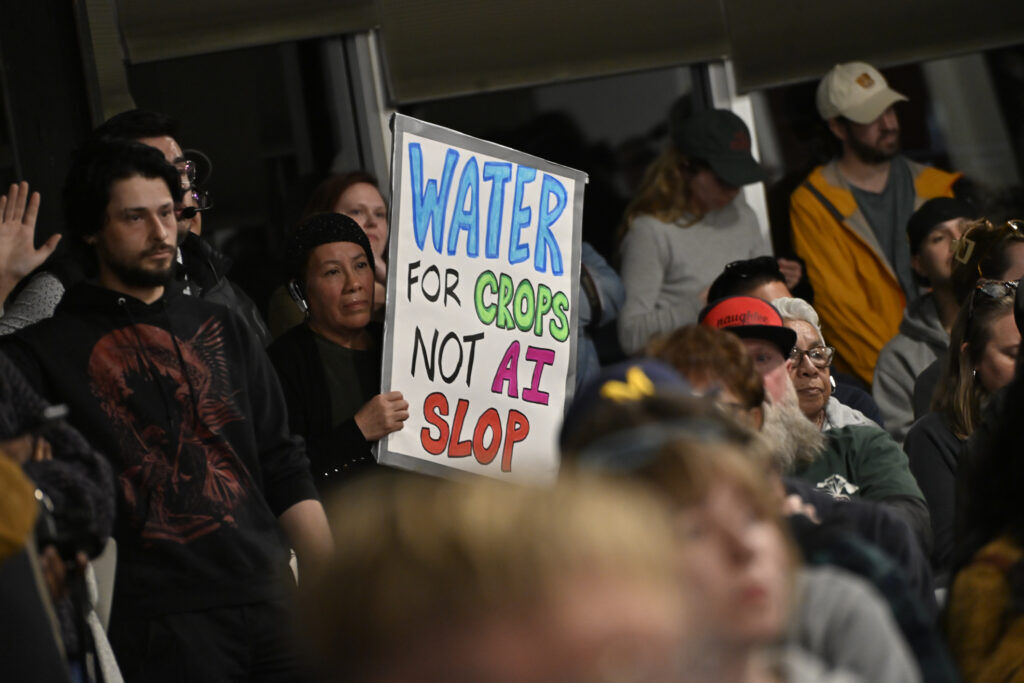 a woman hold a sign at a community meeting about data centers