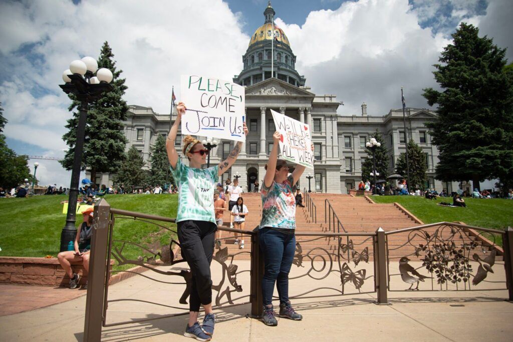 two women holding sign during a protest in front of the state capitol building