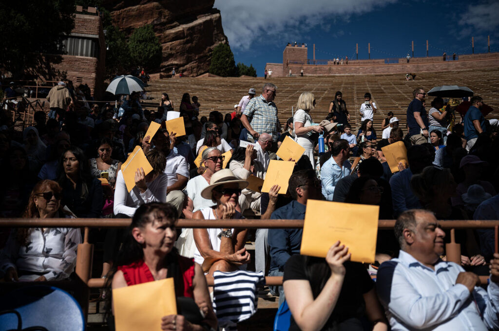 People use their citizenship papers to shield their eyes from the sun as they wait for the start of a naturalization ceremony at Red Rocks on Thursday, July 30, 2026.