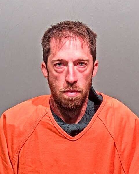 A mugshot of a brunette man in an orange jumpsuit.