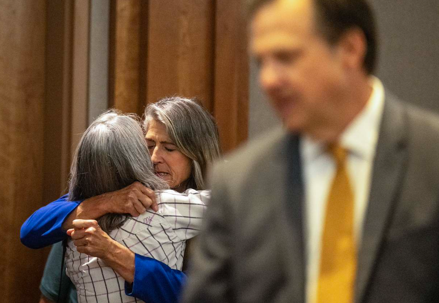 A woman emotionally hugs another in a courtroom